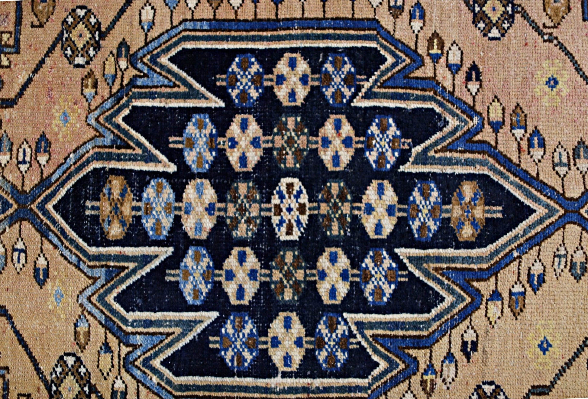 A vintage Persian Mazlaghan rug featuring a dark blue geometric medallion on a tan background.