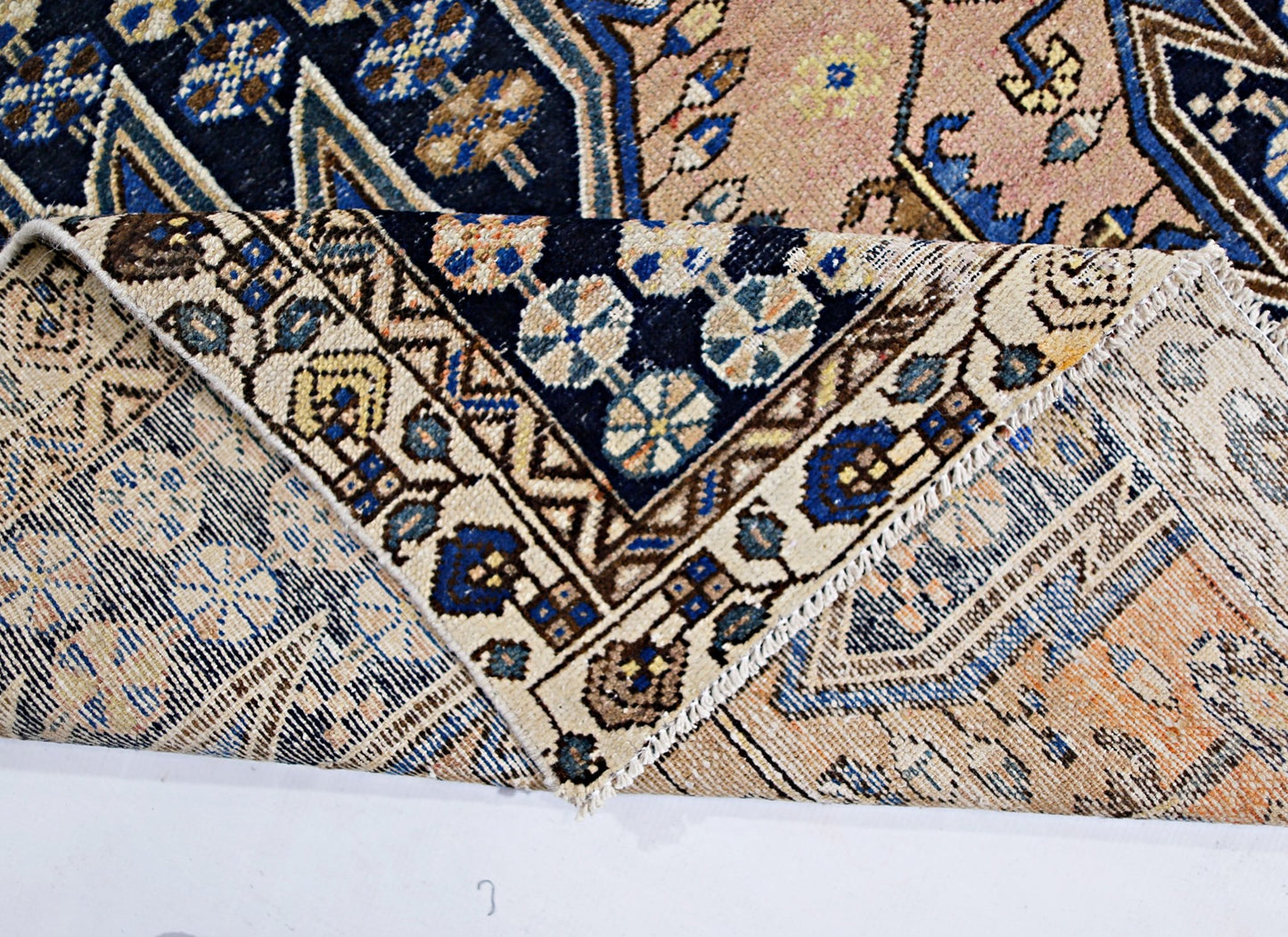 A vintage Persian Mazlaghan rug with a folded corner revealing its intricate geometric patterns.