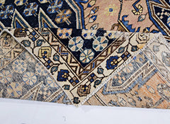 A vintage Persian Mazlaghan rug with a folded corner revealing its intricate geometric patterns.