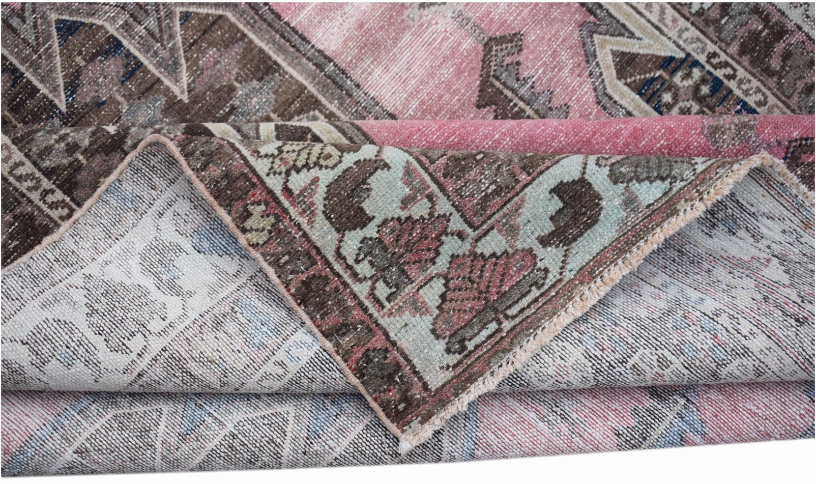 A vintage Persian Mazlaghan rug with a folded corner revealing its intricate floral pattern.