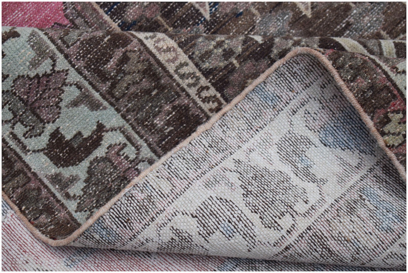 A corner of a vintage handwoven Persian Mazlaghan rug showing its wool pile and cotton backing.