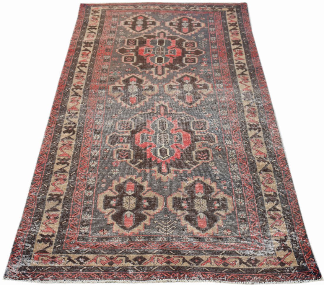 A vintage handwoven Persian rug featuring geometric patterns in shades of red, brown, and grey.