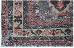 A vintage handwoven Persian rug featuring a geometric pattern in shades of red, black, and beige.