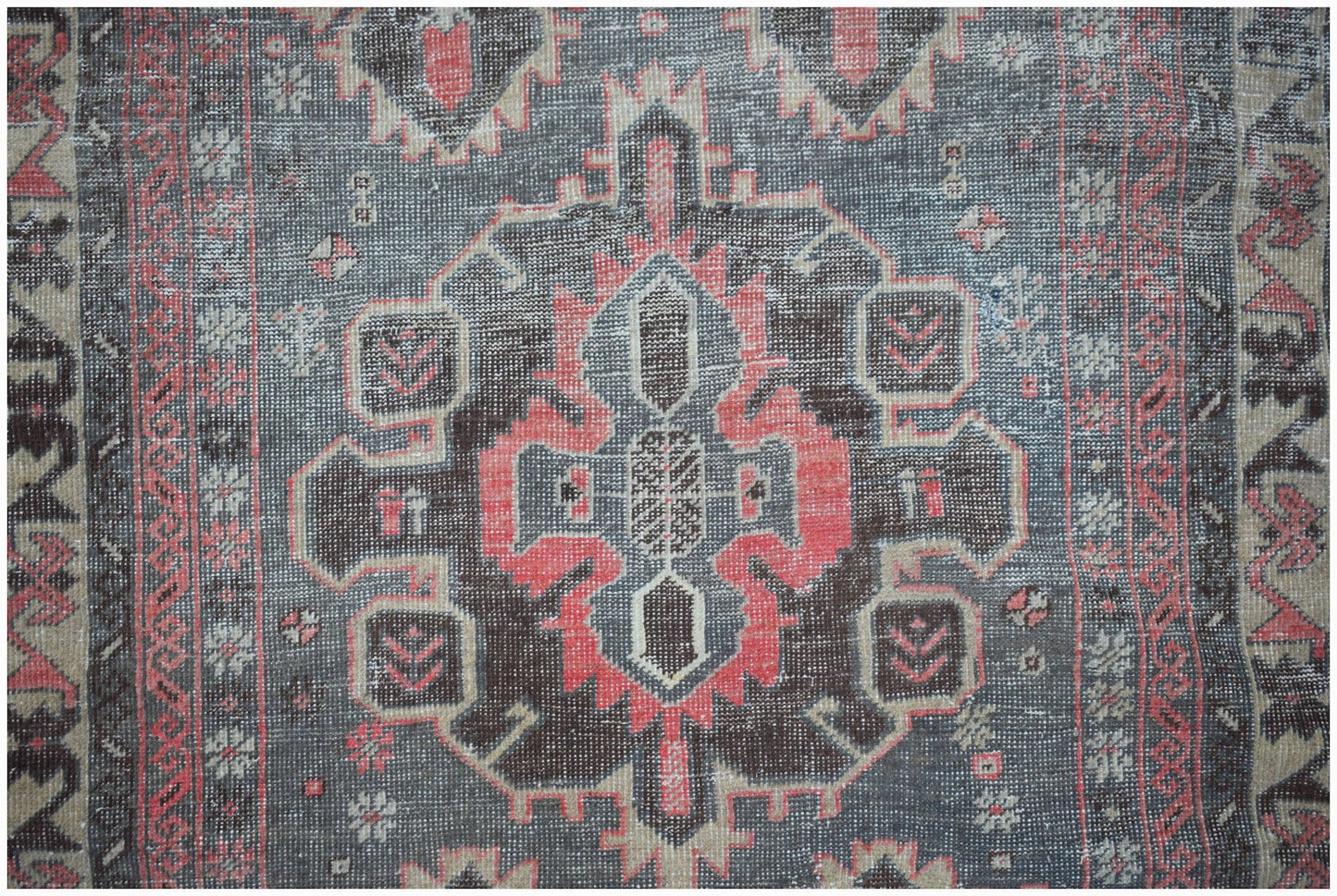 A vintage handwoven Persian rug featuring a geometric medallion in faded red, grey, and beige.