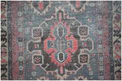 A vintage handwoven Persian rug featuring a geometric medallion in faded red, grey, and beige.