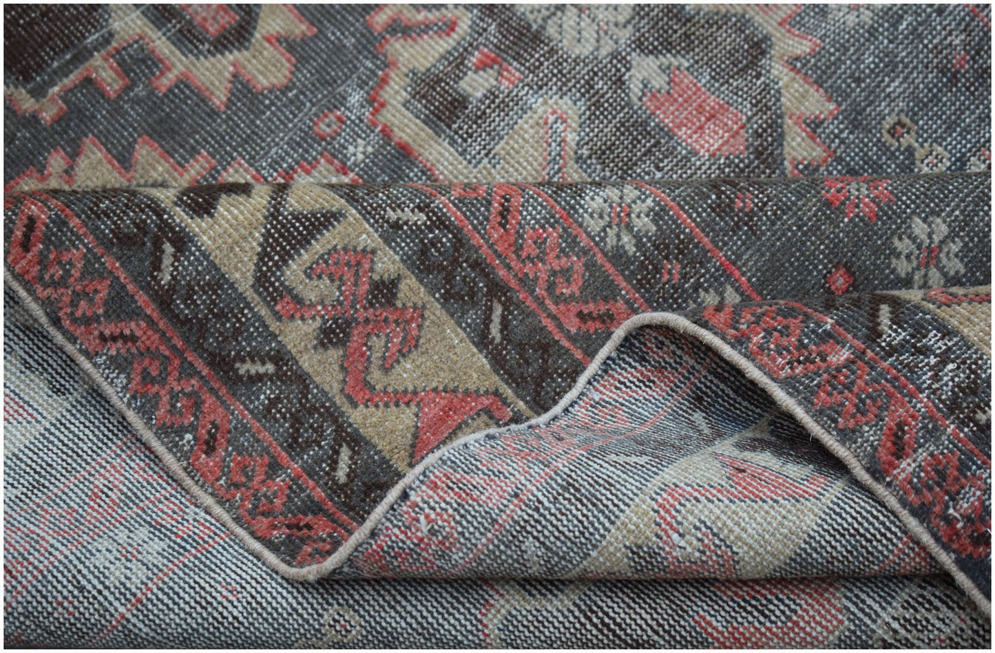 A handwoven vintage Persian rug featuring a distressed geometric pattern in charcoal, tan, and red.