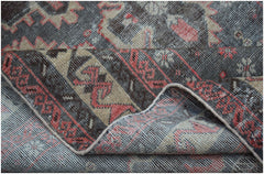 A handwoven vintage Persian rug featuring a distressed geometric pattern in charcoal, tan, and red.