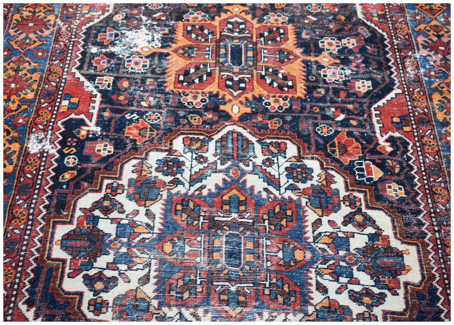 A vintage handwoven Persian rug featuring a traditional geometric pattern in blue, red, and orange.