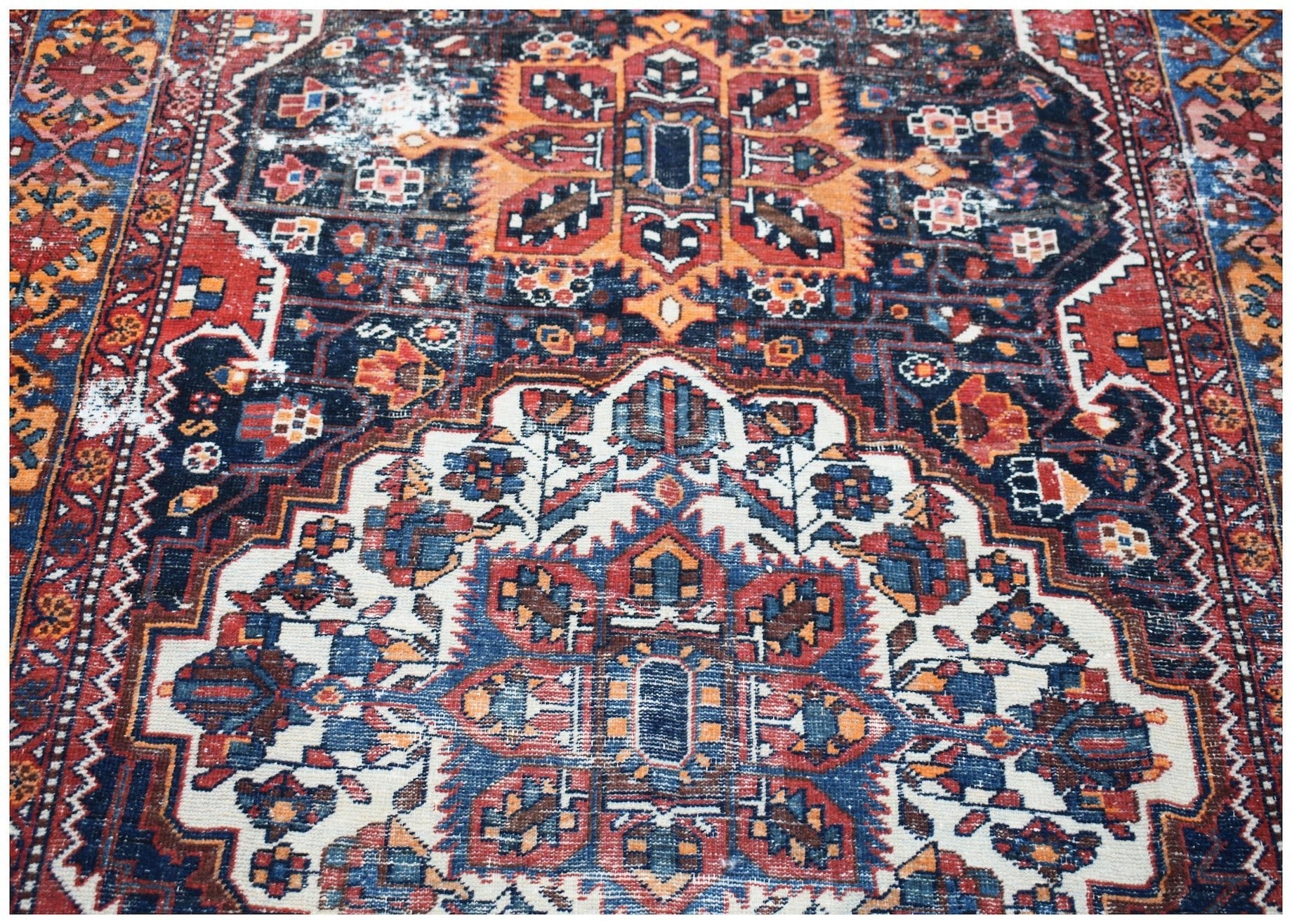 A vintage handwoven Persian rug featuring a traditional geometric pattern in blue, red, and orange.