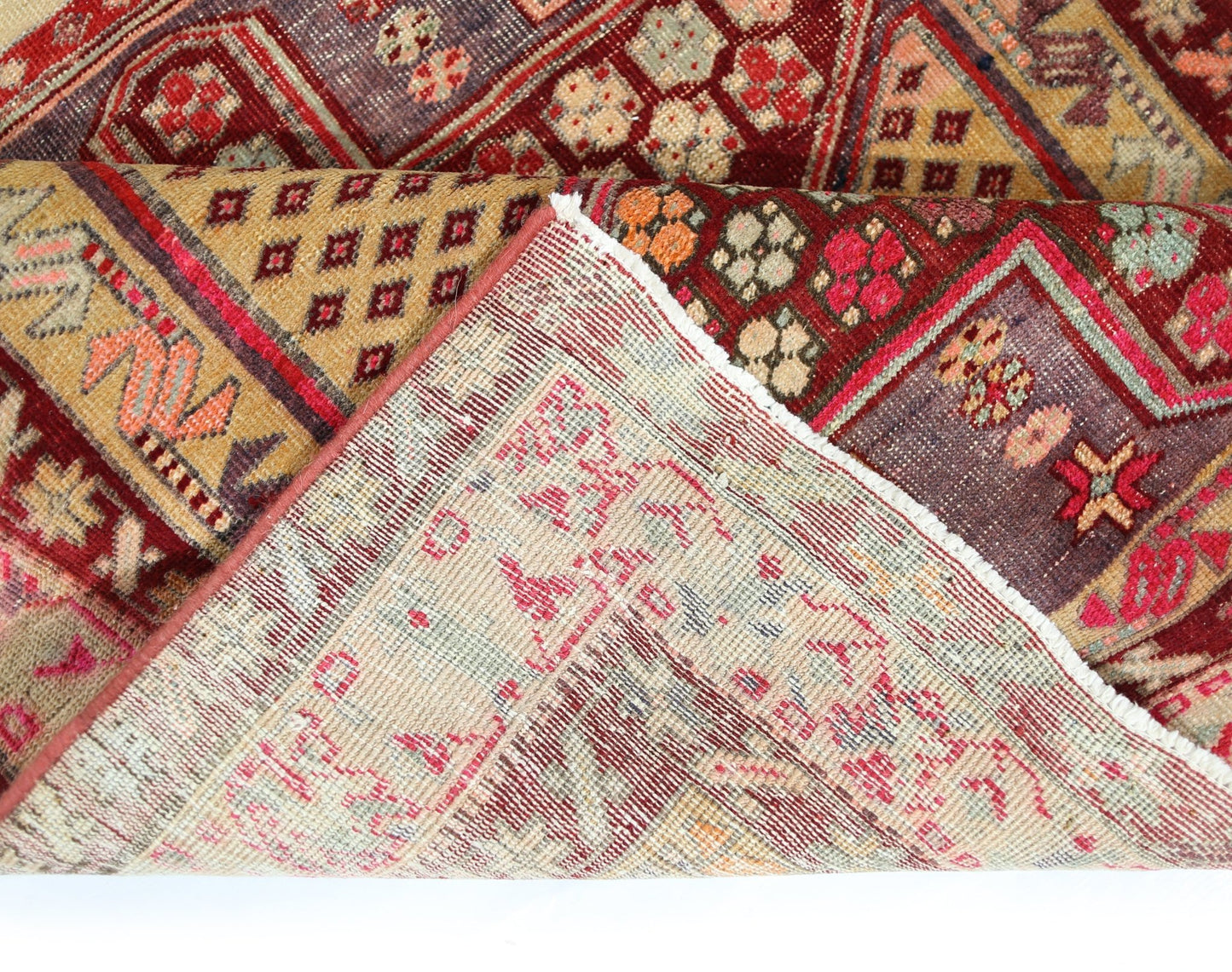 A vintage handmade Persian rug with a geometric floral pattern in red, gold, and purple tones.