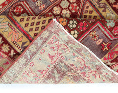 A vintage handmade Persian rug with a geometric floral pattern in red, gold, and purple tones.