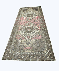 A handmade vintage Persian rug featuring a central floral medallion in shades of pink and grey.