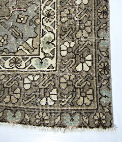 A vintage handmade Persian rug featuring a detailed floral pattern in muted earth tones.