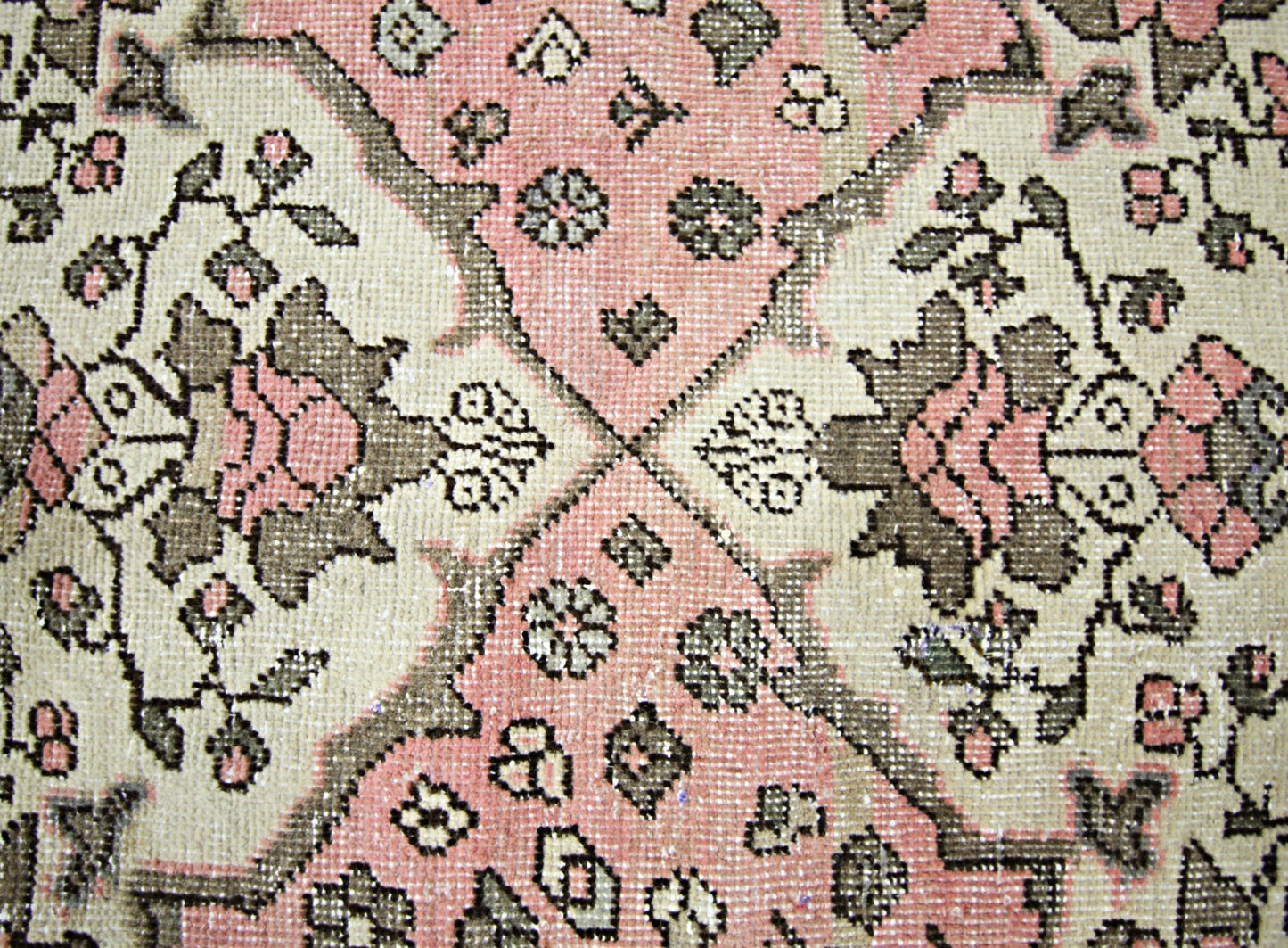 A vintage Persian rug featuring a geometric floral pattern in shades of pink, cream, and grey.