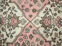 A vintage Persian rug featuring a geometric floral pattern in shades of pink, cream, and grey.