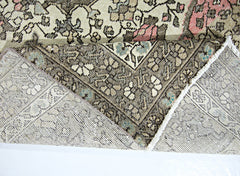 A vintage handmade Persian rug with a floral pattern in muted tones of pink, blue, and brown.