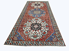 A vintage handmade Persian runner rug featuring a geometric floral pattern in red, blue, and white.