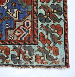 A corner detail of a vintage Persian rug featuring a blue field and a floral light green border.