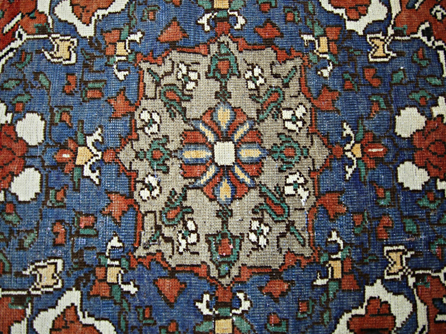 A vintage Persian rug featuring a central floral medallion in a vibrant blue and tan color palette.