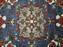 A vintage Persian rug featuring a central floral medallion in a vibrant blue and tan color palette.