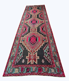 A vintage Persian Ardabil runner featuring geometric medallions in vibrant pink and teal on black.