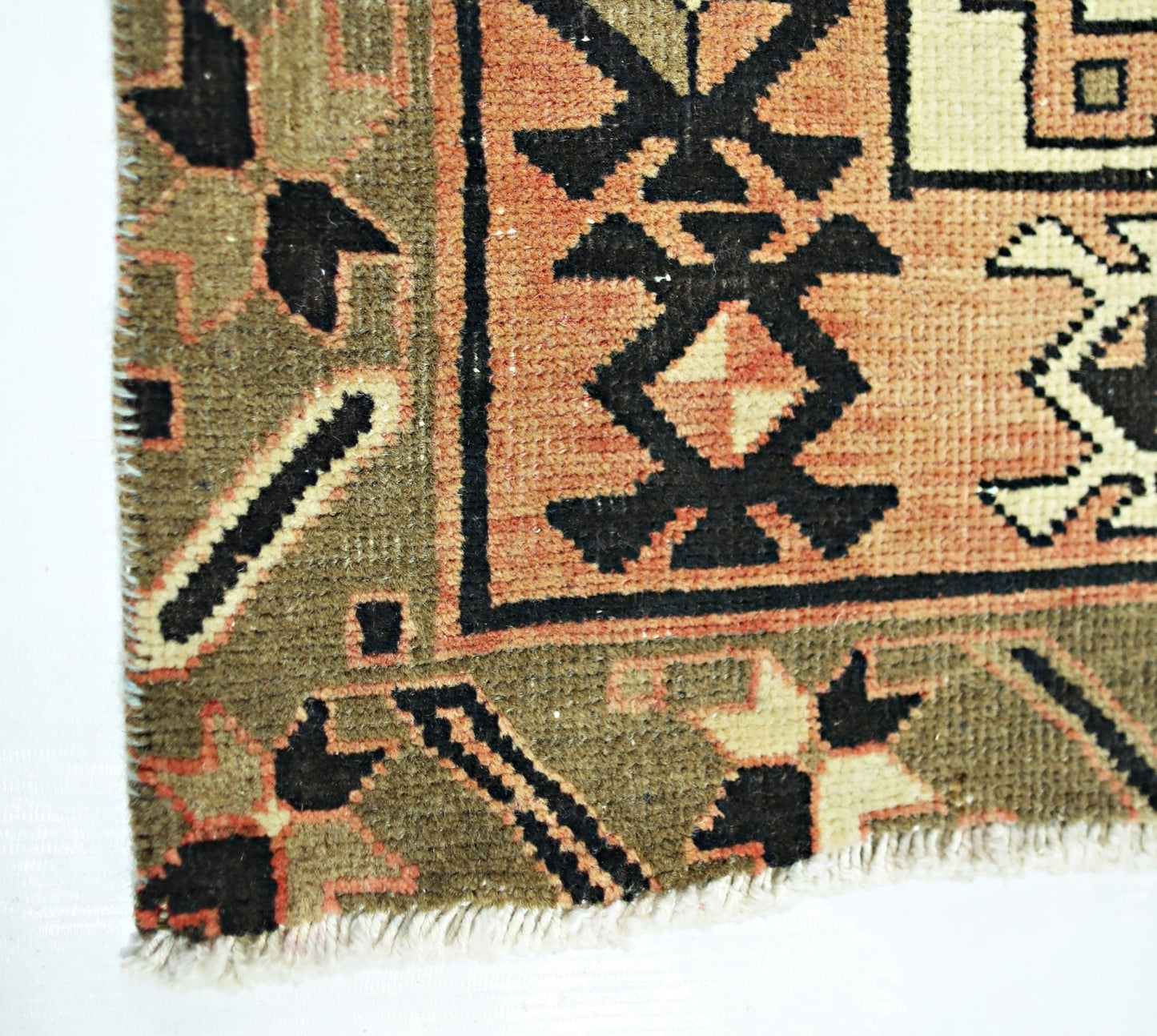 A close-up of a vintage Persian Ardabil runner featuring geometric patterns in olive and peach.