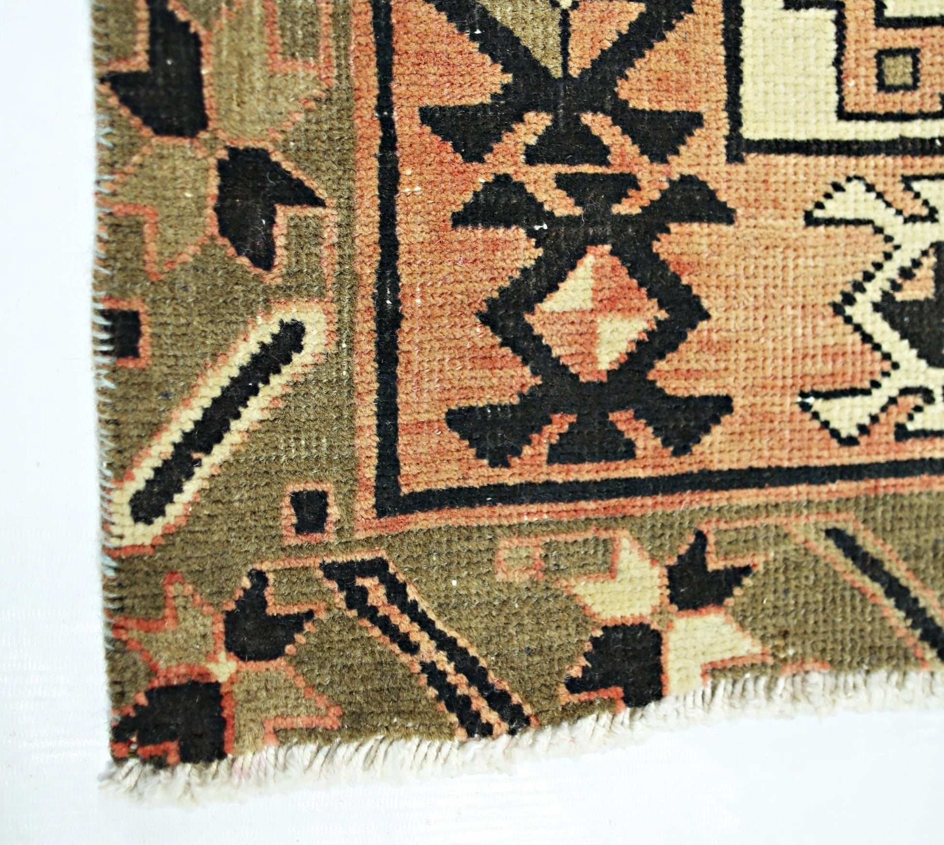 A close-up of a vintage Persian Ardabil runner featuring geometric patterns in olive and peach.