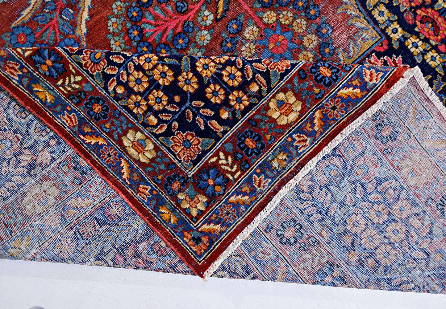 A vintage Persian Moud rug with intricate floral patterns in blue and red, shown folded.