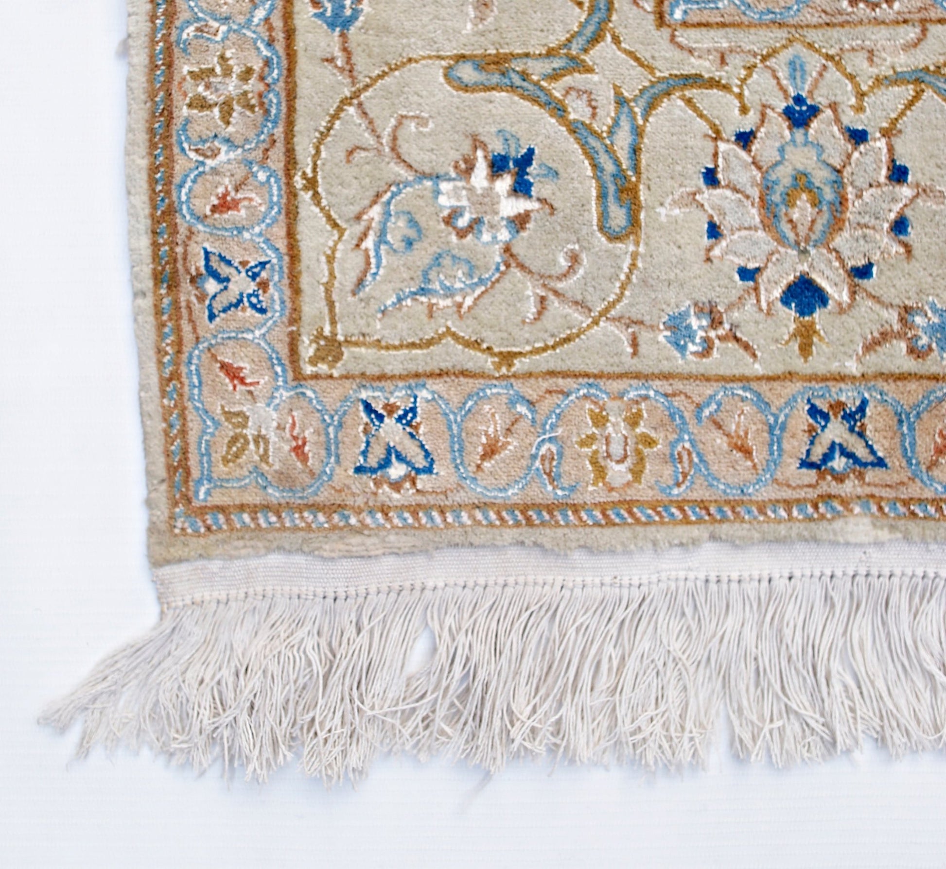 A corner view of a vintage Persian Nain rug featuring intricate floral patterns in blue and beige.