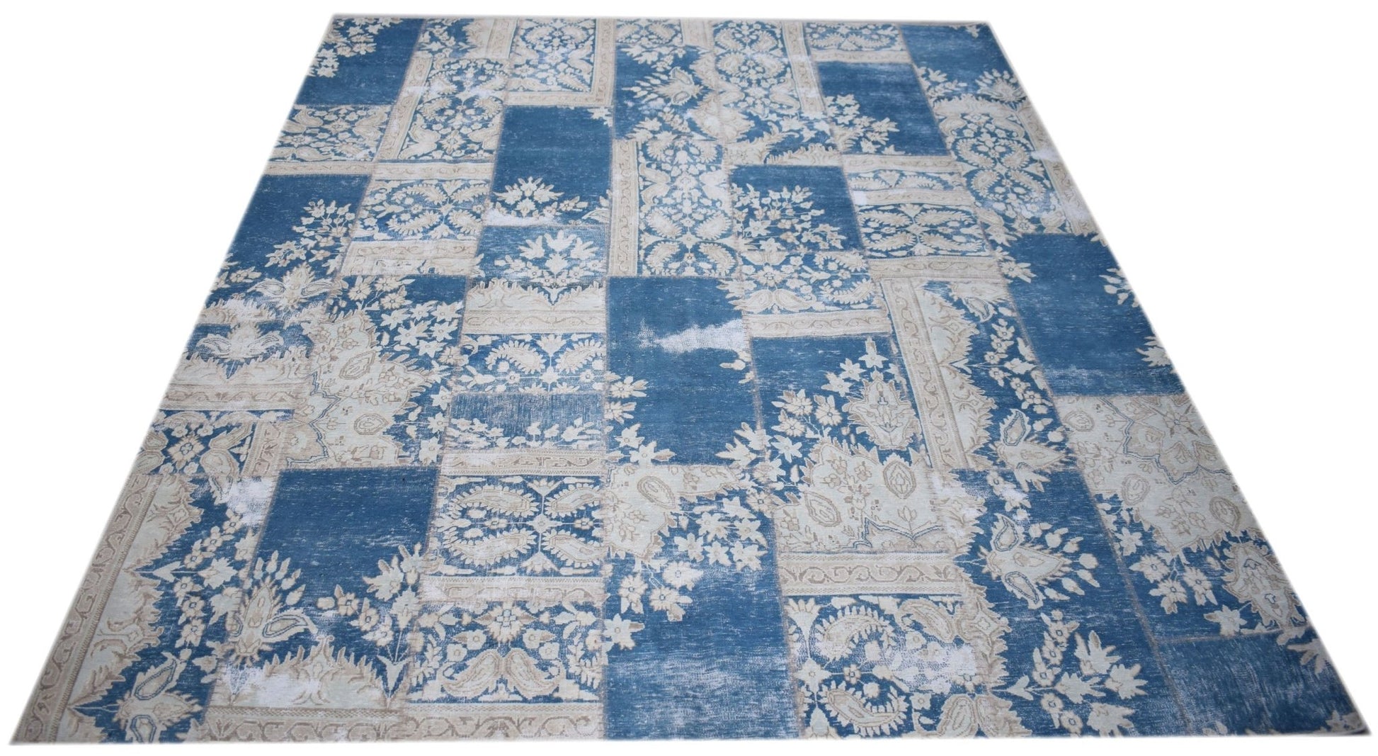 A rectangular handmade wool rug featuring a blue and cream vintage-style patchwork floral pattern.
