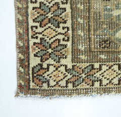 A corner detail of a vintage Persian Qashqai rug featuring intricate floral patterns in muted tones.