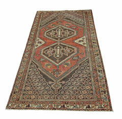 A vintage handmade Persian rug featuring a geometric diamond pattern in red and brown tones.