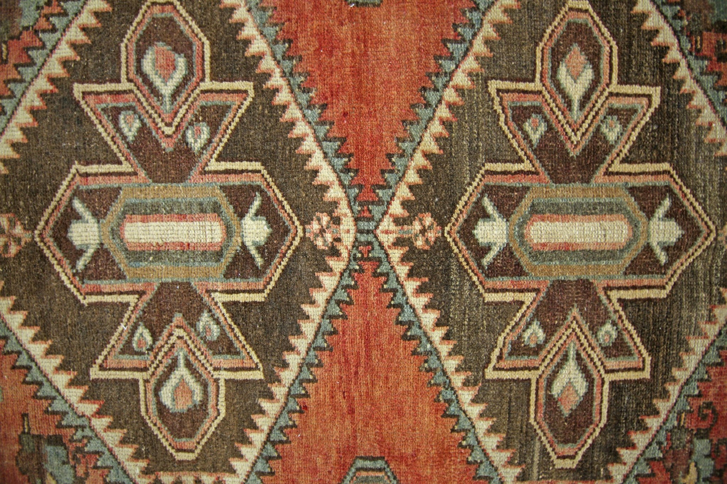 A vintage Persian rug featuring geometric diamond patterns in shades of brown, orange, and blue.