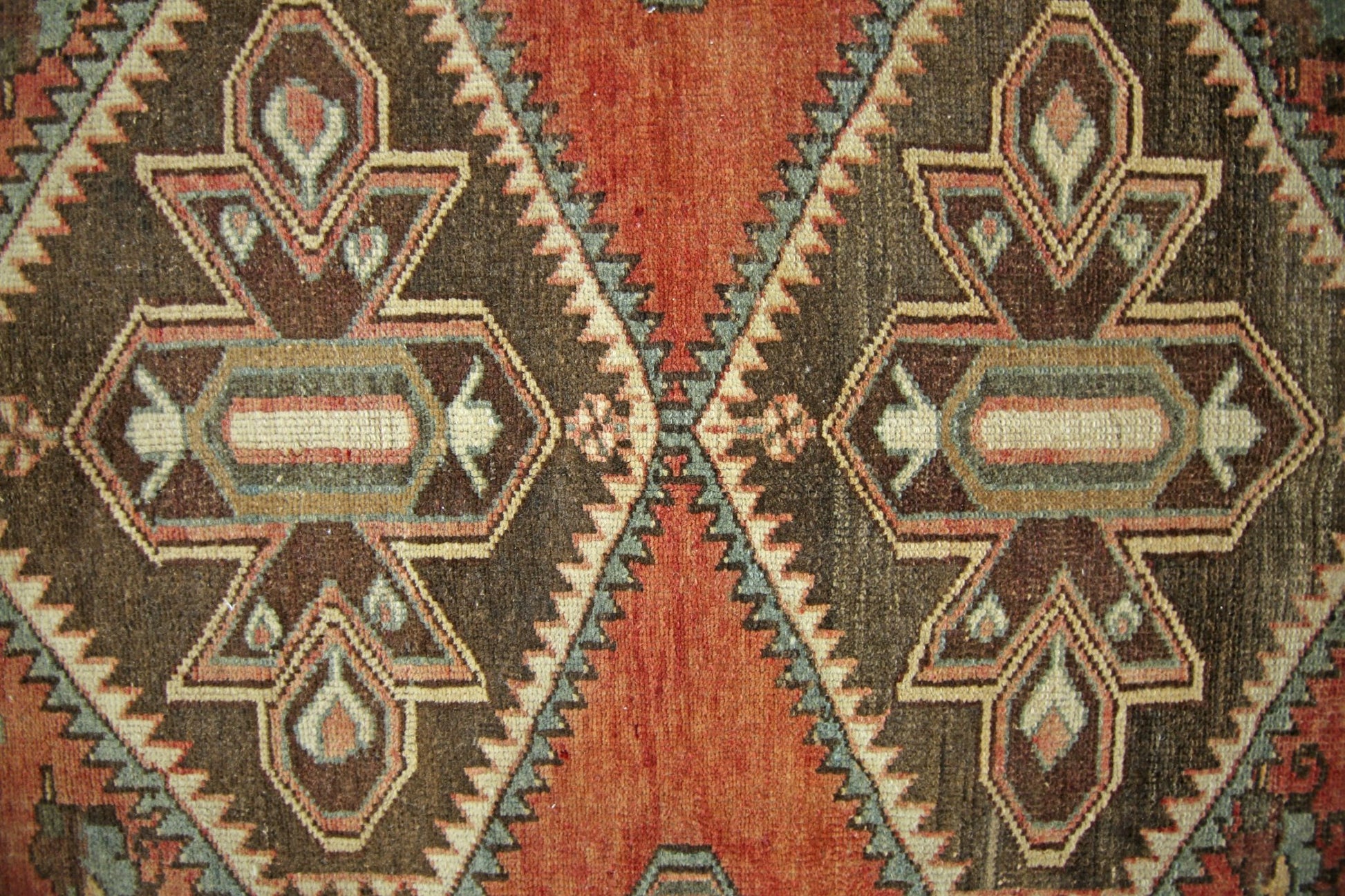 A vintage Persian rug featuring geometric diamond patterns in shades of brown, orange, and blue.