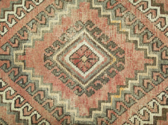 A vintage Persian rug featuring a geometric diamond pattern in shades of red, grey, and cream.