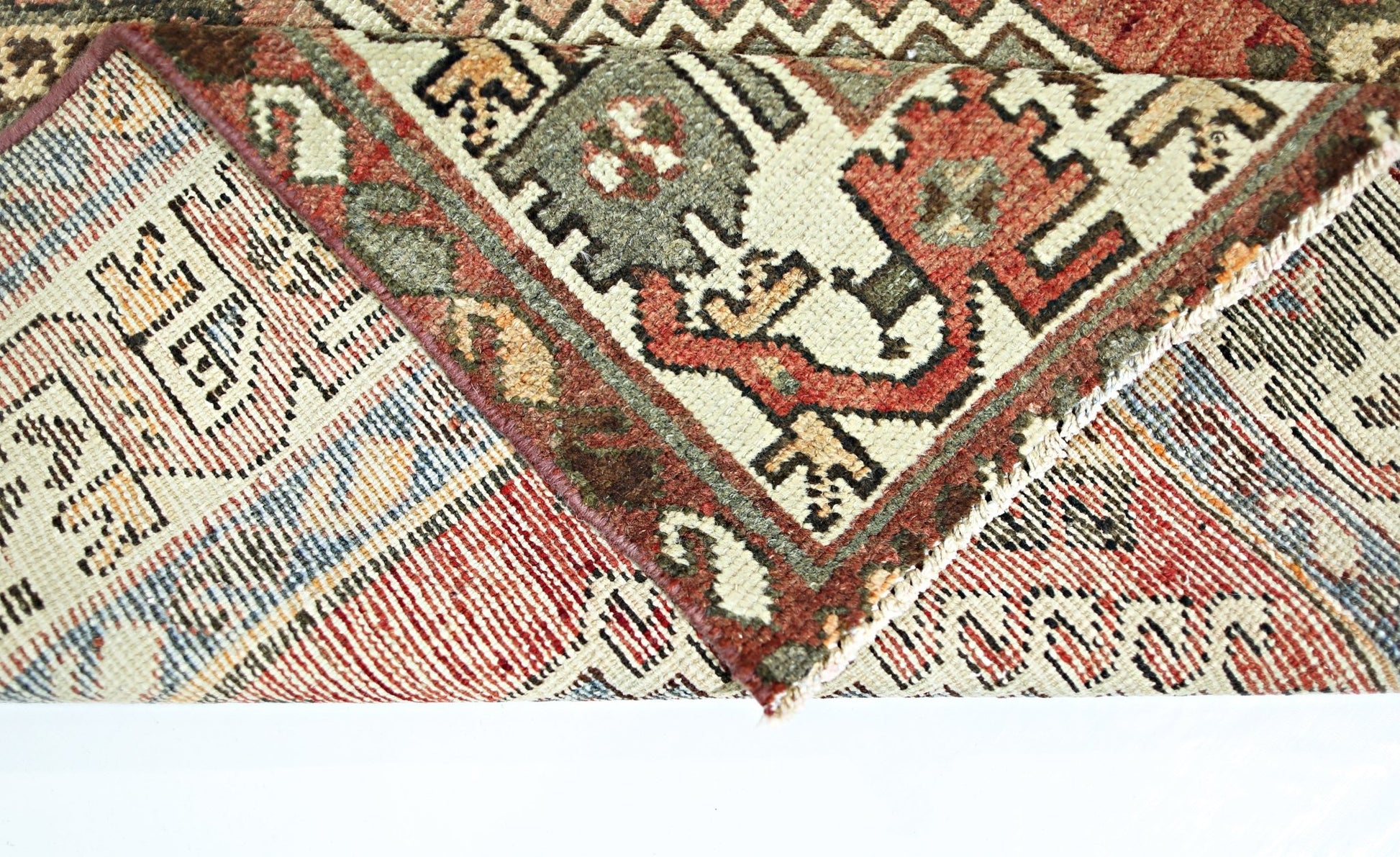 A folded vintage Persian rug featuring intricate geometric patterns in red, green, and cream.