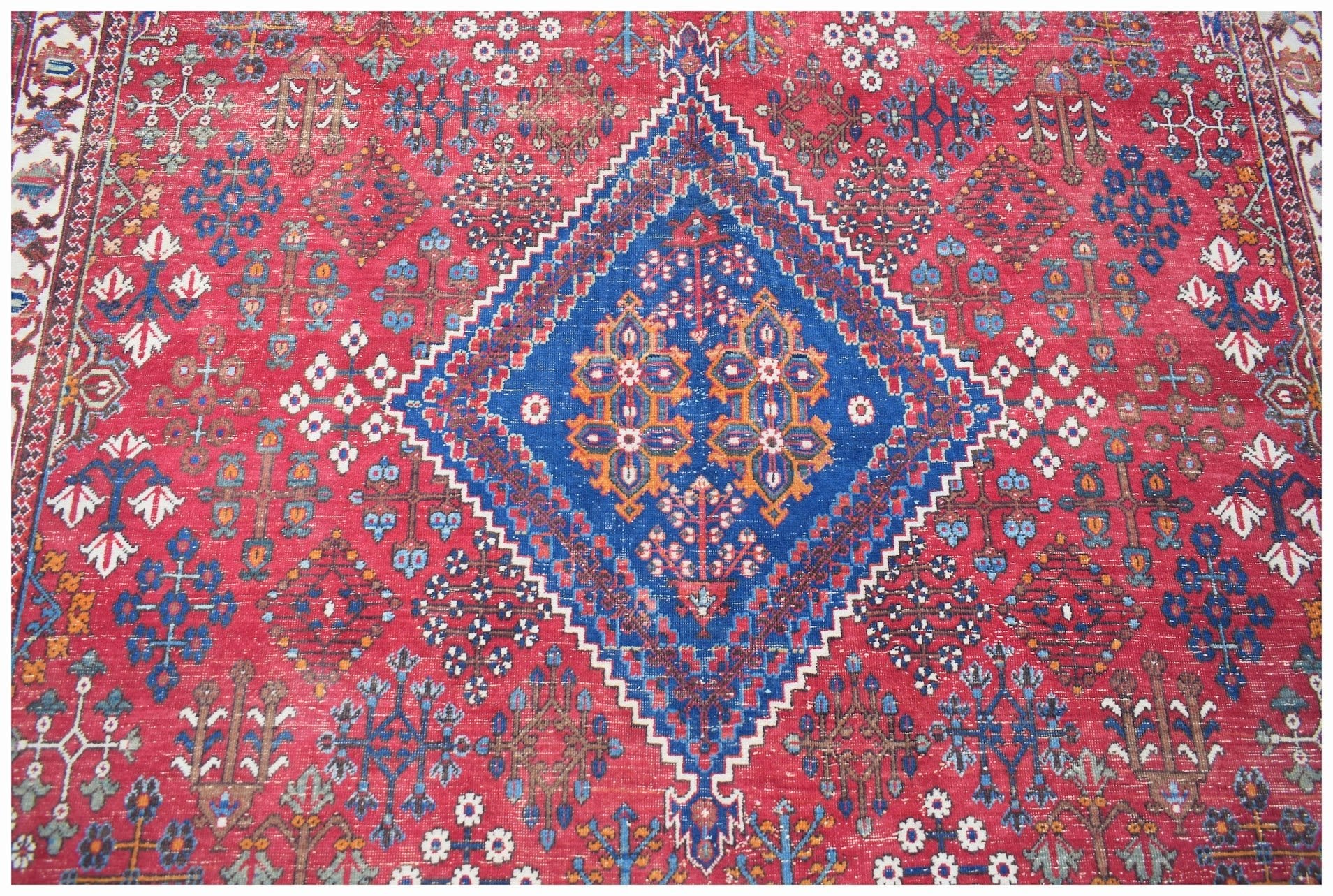 A vintage handwoven Persian Ghashghai rug featuring a large blue diamond medallion on a red field.