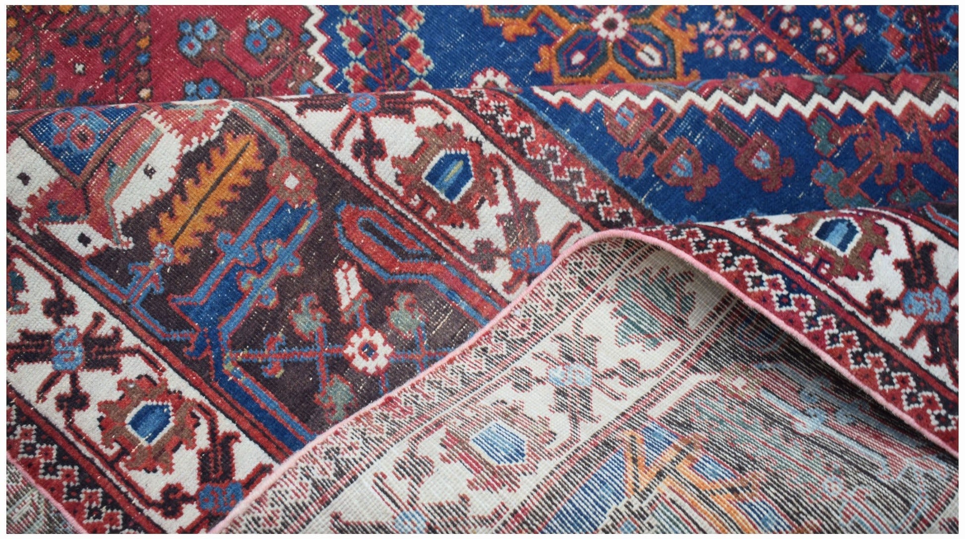 A folded vintage Persian Ghashghai rug featuring intricate geometric patterns in red and blue.