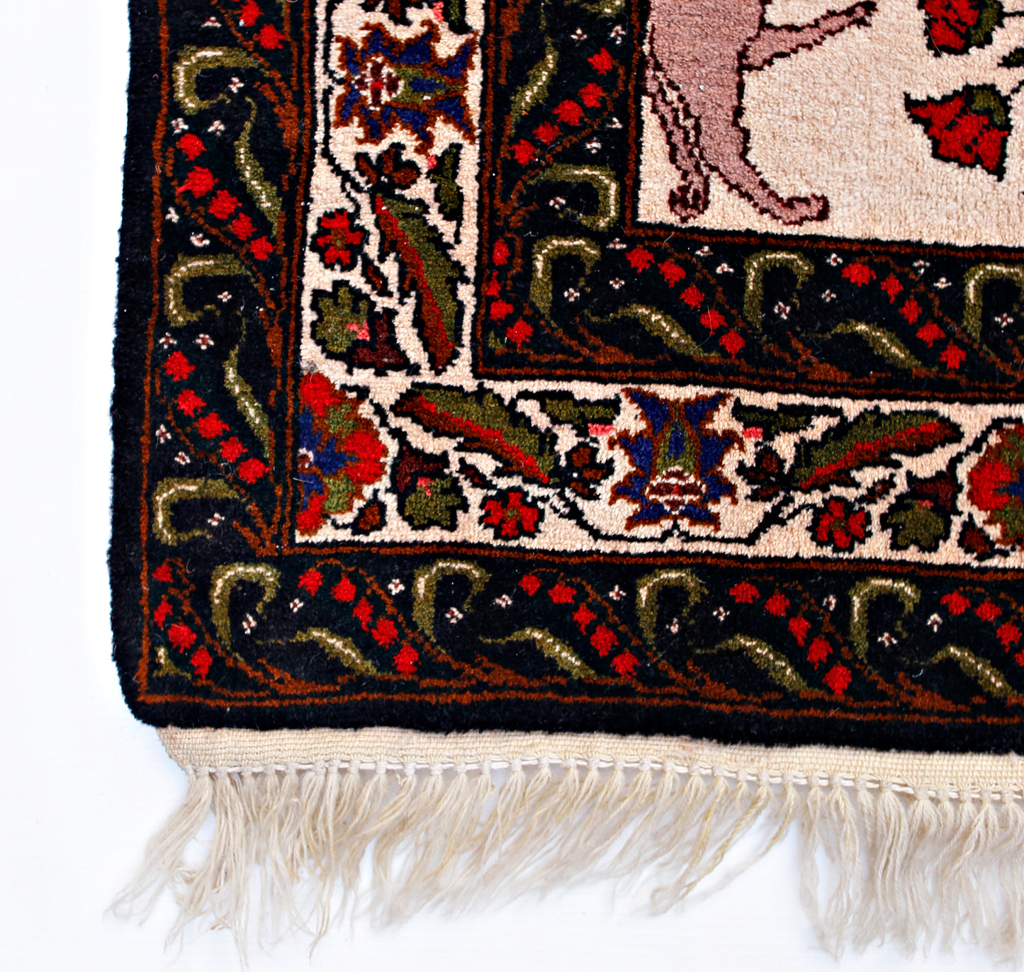 A corner detail of a vintage Persian rug featuring a hunting scene with intricate floral borders.