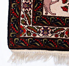 A corner detail of a vintage Persian rug featuring a hunting scene with intricate floral borders.