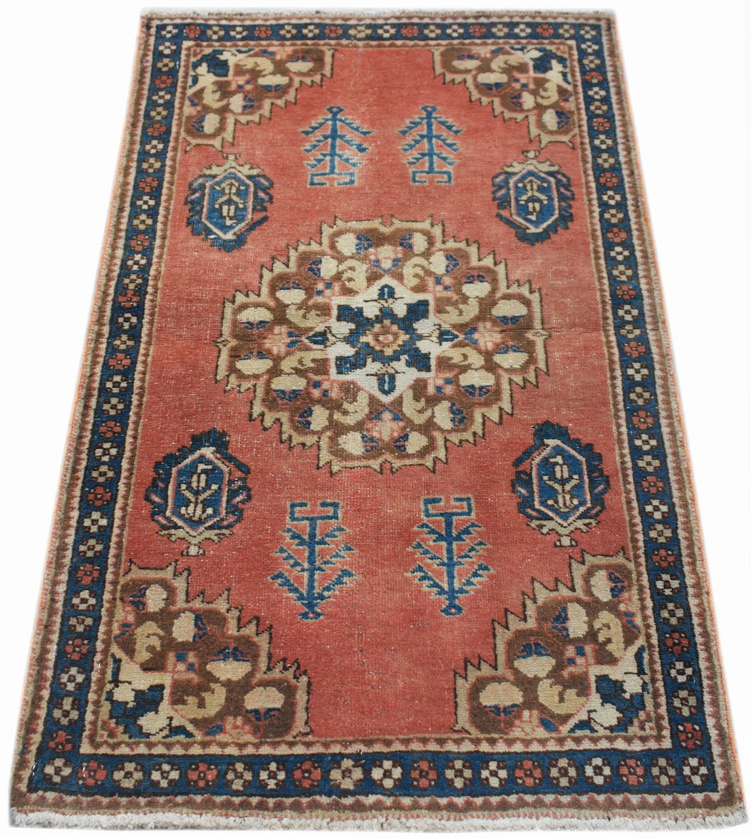 A vintage handwoven Persian rug featuring a central medallion on a faded red field with blue borders.