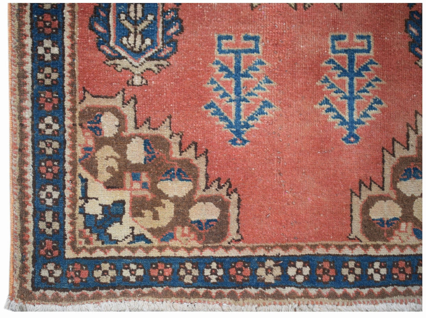 A vintage handwoven Persian rug featuring a coral field with blue floral motifs and geometric borders.