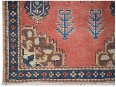 A vintage handwoven Persian rug featuring a coral field with blue floral motifs and geometric borders.