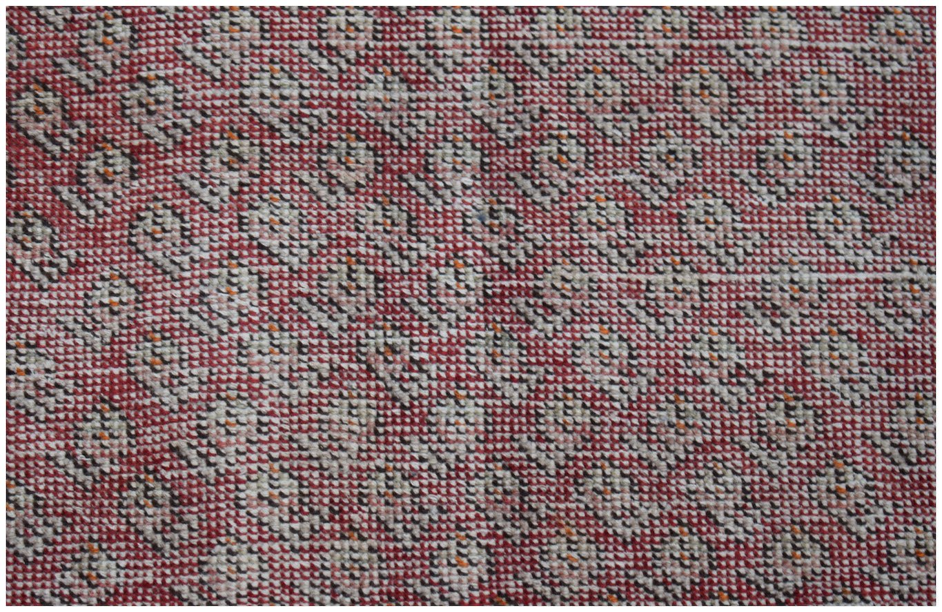 A vintage Persian rug featuring a repeating geometric pattern in shades of red, cream, and black.