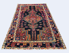 A vintage handmade Persian rug featuring a geometric medallion pattern in red, blue, and black.