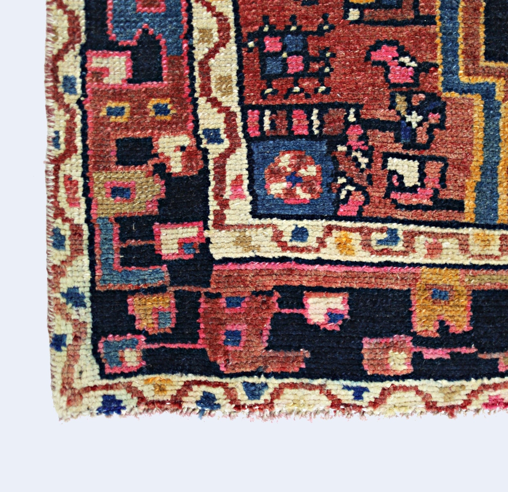 A corner view of a vintage handmade Persian rug featuring geometric patterns in red and blue.