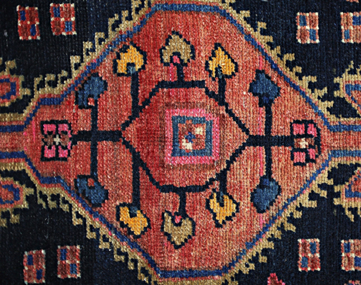 A vintage Persian rug featuring a central geometric medallion in red, blue, and gold wool.