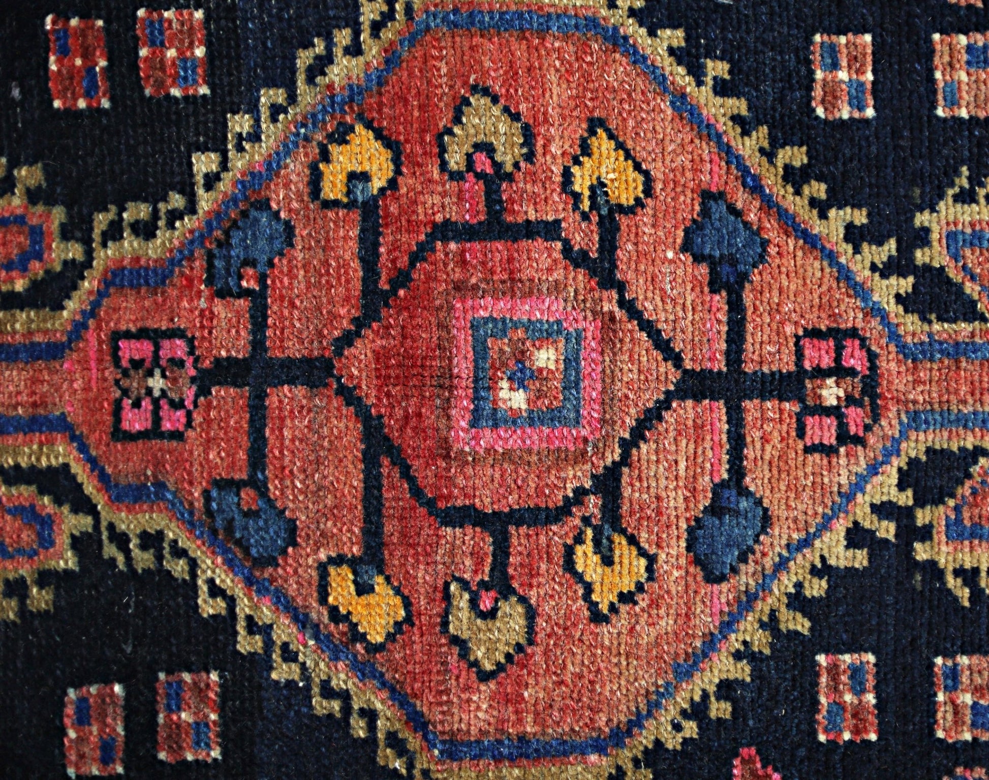 A vintage Persian rug featuring a central geometric medallion in red, blue, and gold wool.