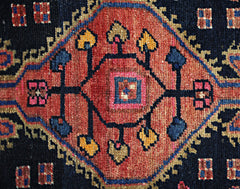 A vintage Persian rug featuring a central geometric medallion in red, blue, and gold wool.
