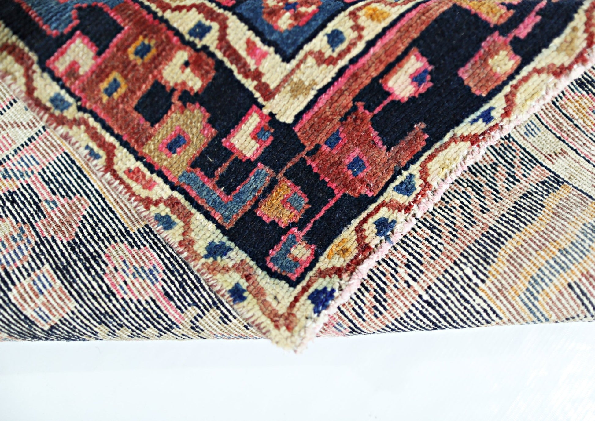 A corner of a vintage handmade Persian wool rug showing its intricate geometric pattern and weave.